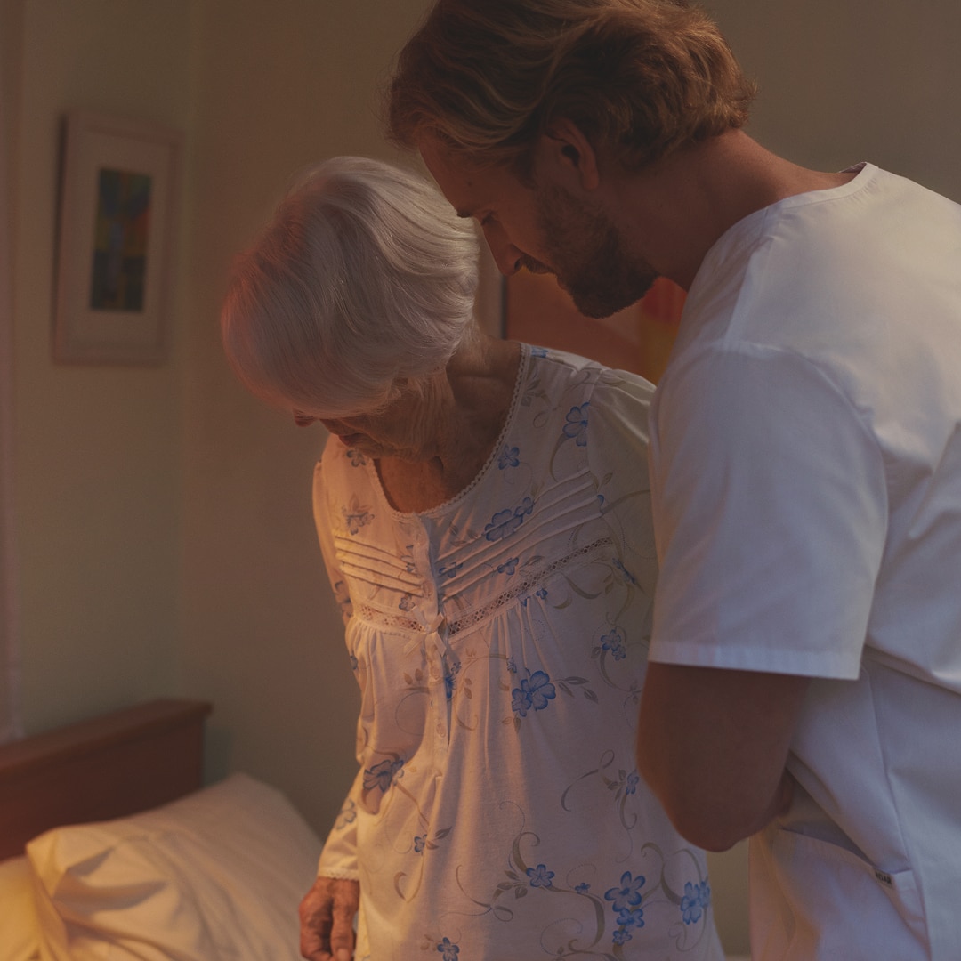 A male nurse is helping an old lady to bed.