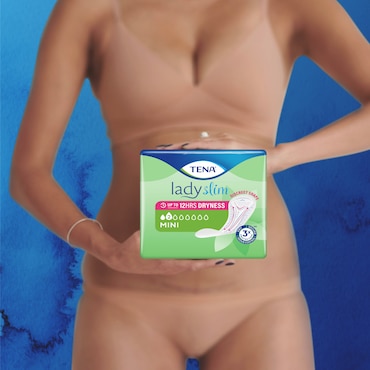 Biała kobieta w beżowej bieliźnie, z pierścionkami na palcach, trzymająca opakowanie TENA Lady Mini przed sobą.