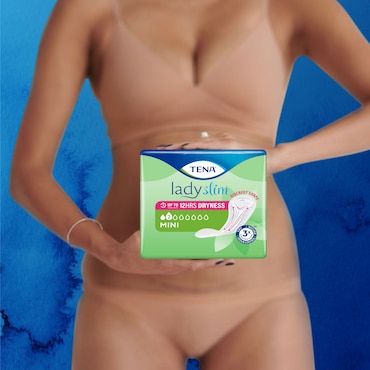 Biała kobieta w beżowej bieliźnie, z pierścionkami na palcach, trzymająca opakowanie TENA Lady Mini przed sobą.