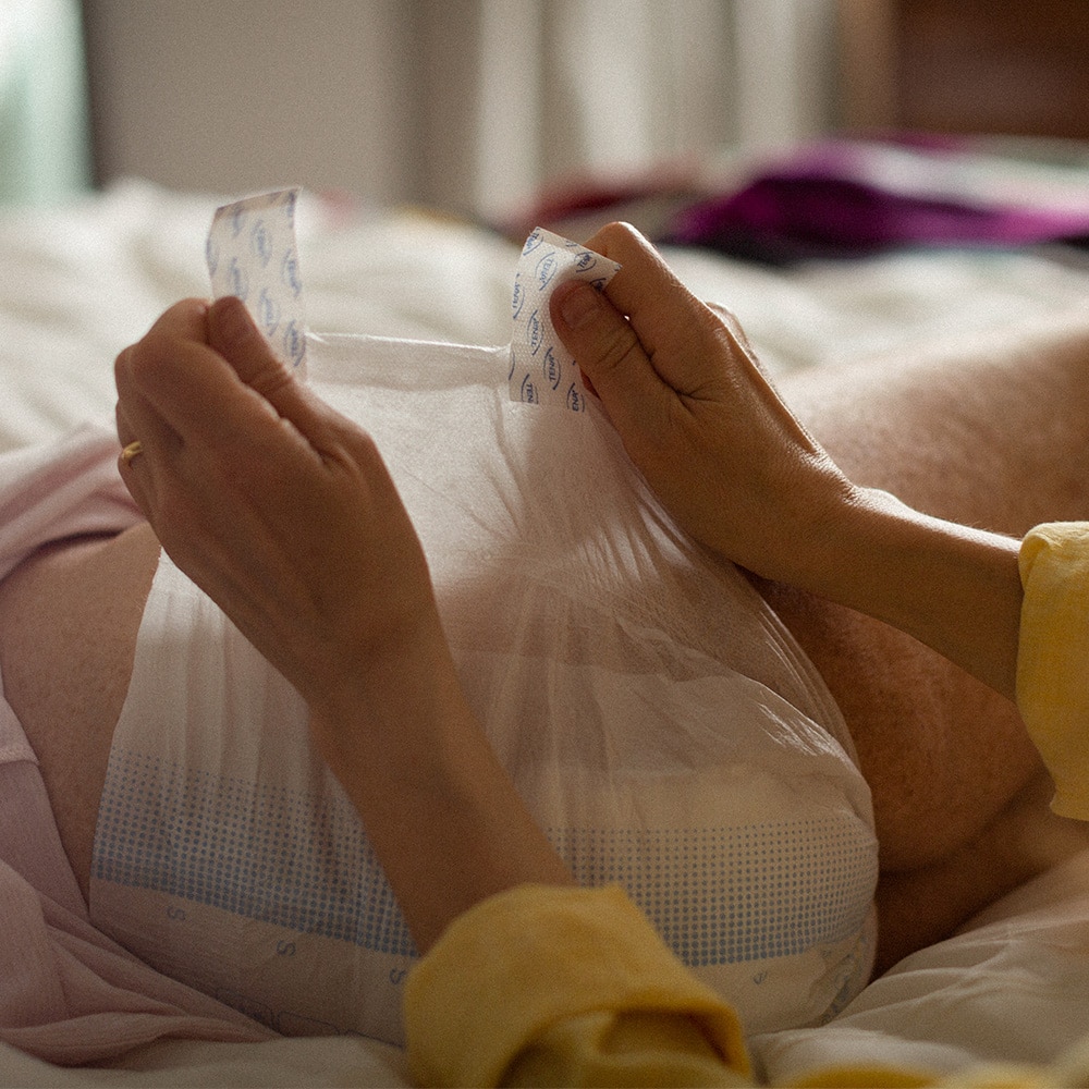Close-up of a carer securing TENA Flex onto a user who is lying down on their side