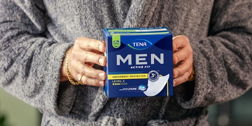 Model de sex masculin în halat de baie care ține un pachet de absorbante TENA. 