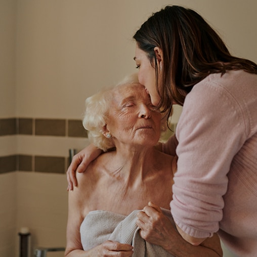 Uma mulher beija gentilmente uma idosa na testa.