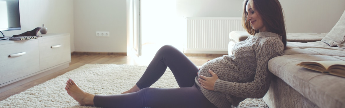 Siedząca na podłodze kobieta w ciąży, obejmująca swój brzuch