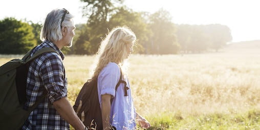 Homme et femme d’âge mûr avec des sacs à dos se promenant dans un champ ensoleillé