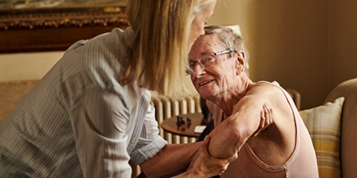 A caregiver helps an older man stand up