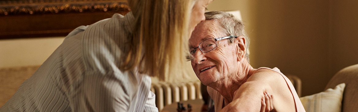 A caregiver helps an older man stand up