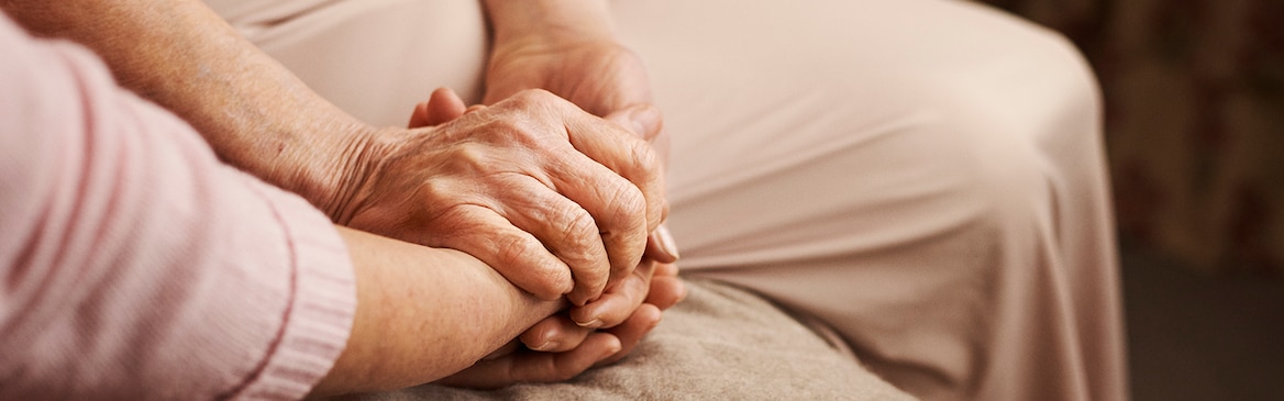 Close-up of an incontinent woman and her carer holding hands