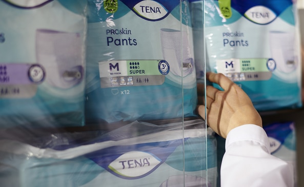La main tendue vers un paquet de TENA ProSkin Pants sur une étagère de magasin.
