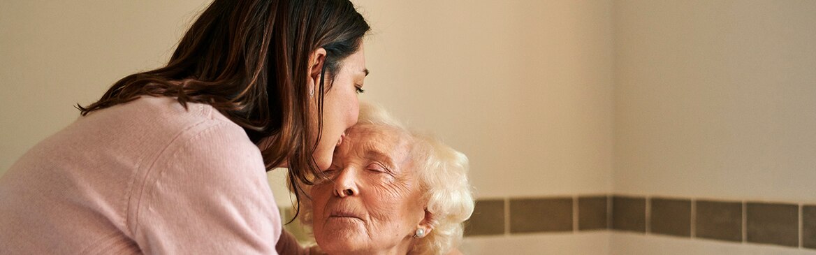 Äldre kvinna får en puss på huvudet av vårdgivare.