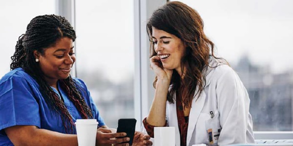 Twee vrouwelijke professionele zorgverleners controleren hun berichten in de TENA SmartCare Professional Care-app