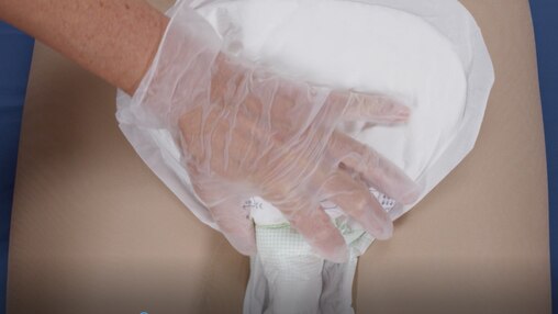 Кадр из видеоролика, в котором ухаживающий за близким помогает надеть подопечному с ограниченной подвижностью прокладку TENA.