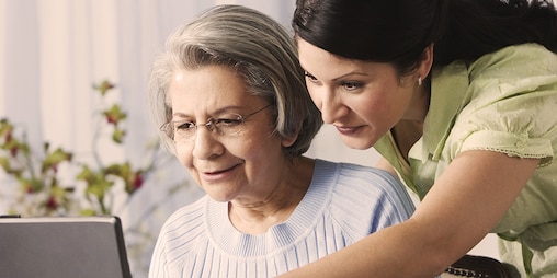 Ηλικιωμένη γυναίκα και νέα γυναίκα που χρησιμοποιούν υπολογιστή - πώς η νόσος Alzheimer επηρεάζει το αγαπημένο σας πρόσωπο