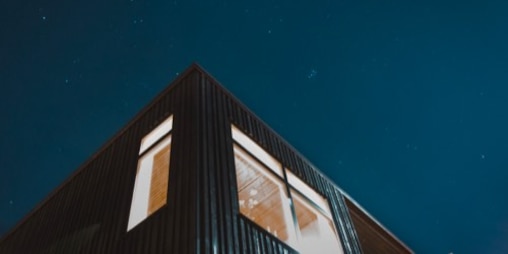 Gece vakti üzerinde yıldızlarla dolu berrak bir gökyüzü bulunan bir evin köşesinin alttan görünümü 
