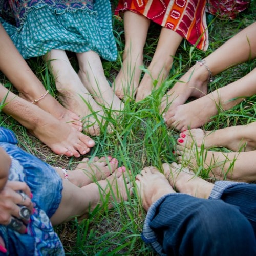Bare feet of a group of young girls in a circle on green grass. 