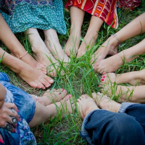 Bare feet of a group of young girls in a circle on green grass. 