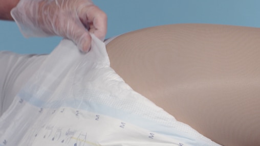 Fermo immagine del video in cui un caregiver aiuta il proprio caro in posizione supina a indossare TENA Flex.
