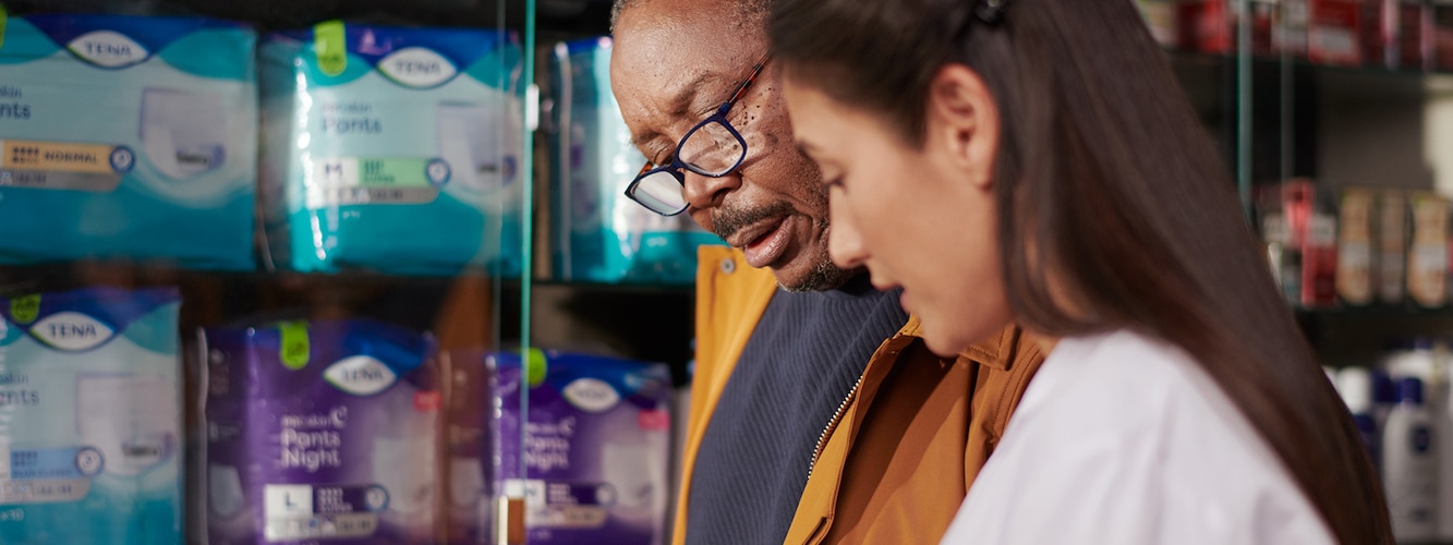 A female pharmacist talks to a male customer about the TENA Men range. 