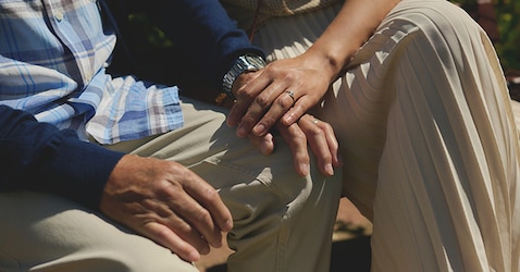 An elderly man and a woman holding hands outside.