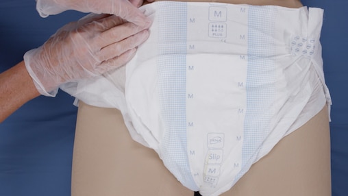 Snímek z videa o pečovateli, který obléká plenkové kalhotky TENA Slip ležícímu uživateli.