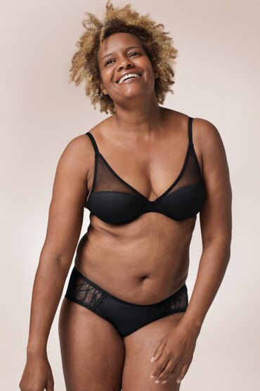 White woman wearing a black bra and a pair of TENA Silhouette Washable Absorbent Underwear in a Hipster brief. 