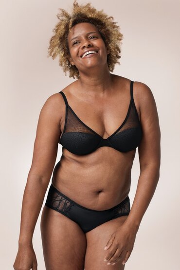 Afroamerikanische Frau, die einen schwarzen BH und die TENA Silhouette waschbare Unterwäsche in der Hipster-Variante trägt.
