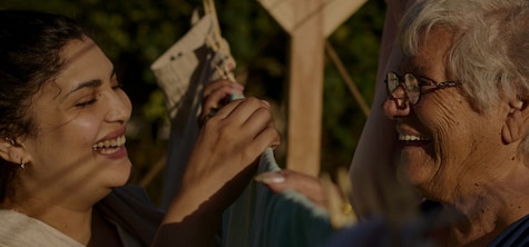 Two smiling women with age difference hanging clothes on washing line outdoors