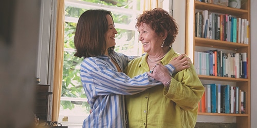 Une jeune femme étreint une femme plus âgée. Toutes deux sourient.