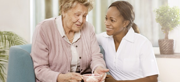 Une femme âgée boit du thé et discute avec un soignant.