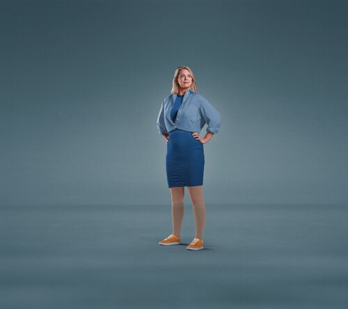 A woman standing against a plain blue background with both hands on her hips, dressed in a blue shirt, blue skirt, and orange shoes, wearing Knee-high JOBST Relief compression stockings.
