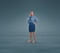 A woman standing against a plain blue background with both hands on her hips, dressed in a blue shirt, blue skirt, and orange shoes, wearing Knee-high JOBST Relief compression stockings.