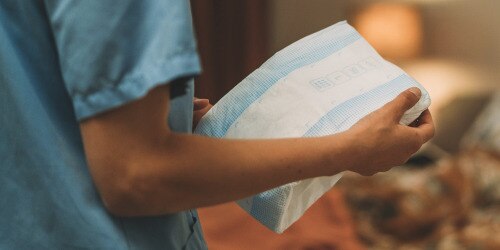 Immagine ravvicinata delle mani di un caregiver professionista mentre tiene in mano un prodotto assorbente TENA