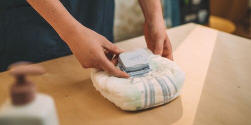 Een close-up van de handen van een professionele zorgverlener die de TENA SmartCare Identifi logger aanbrengt op de voorkant van een TENA incontinentieverband