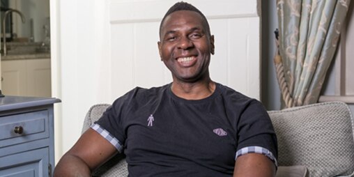 Luke Williams a prostate cancer survivor sat on sofa smiling