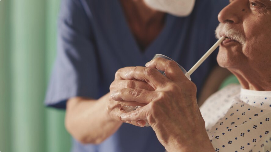 A professional caregiver helps a nursing home resident take a drink using a straw.