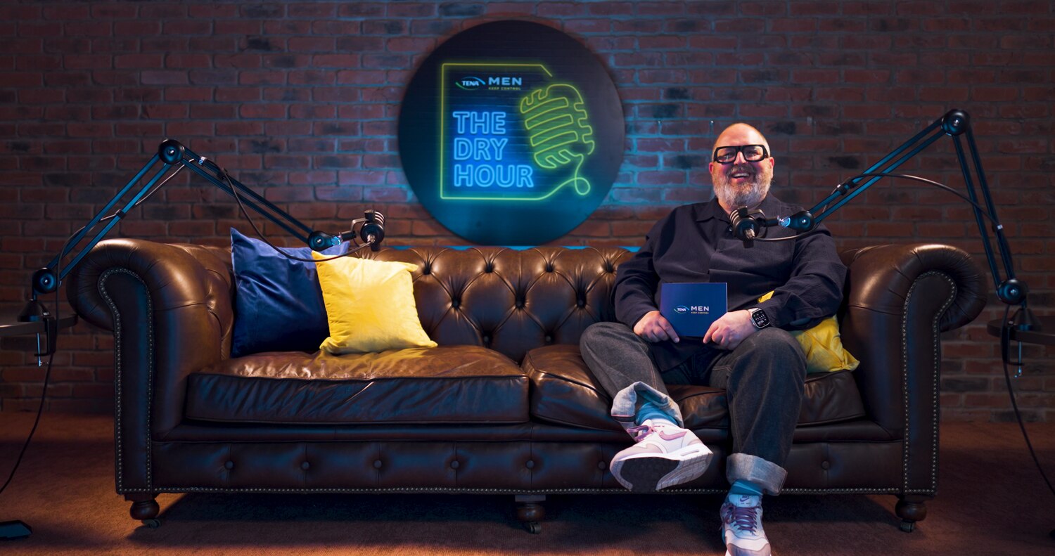 Comedian Justin Moorhouse sat on a sofa in front of Dry Hour TENA logo