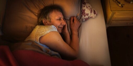 An elderly woman sleeps soundly in her bed.