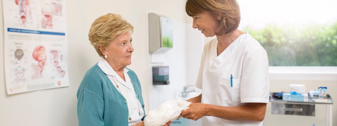 Une médecin dans son bureau montre à sa patiente âgée comment changer son nouveau produit d’incontinence.