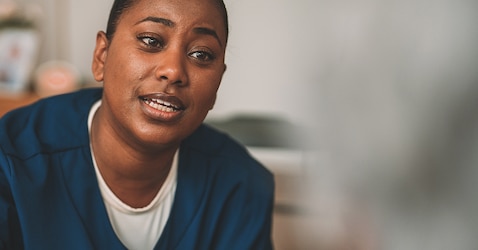 A female professional caregiver wearing a blue uniform talks in a nursing home environment 