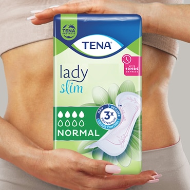 A white woman wearing beige underwear and rings, holding a TENA SlimMini pack in front of her.