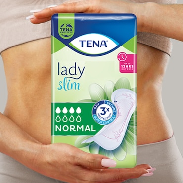 A white woman wearing beige underwear and rings, holding a TENA SlimMini pack in front of her.