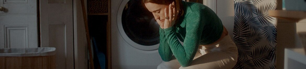 Een vermoeide vrouw die alleen in een wasruimte zit.