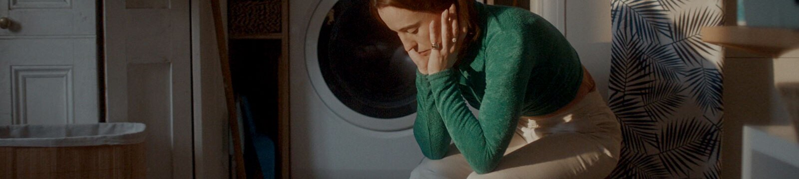 An exhausted woman sits alone in a laundry room