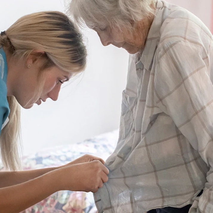 Eine Pflegerin knüpft das Hemd einer Bewohnerin zu