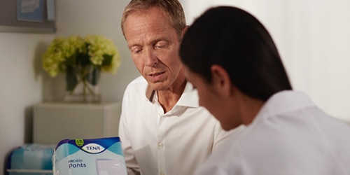 En farmaceut i en samtale med en TENA-repræsentant, der forklarer fordelene ved et produkt. 