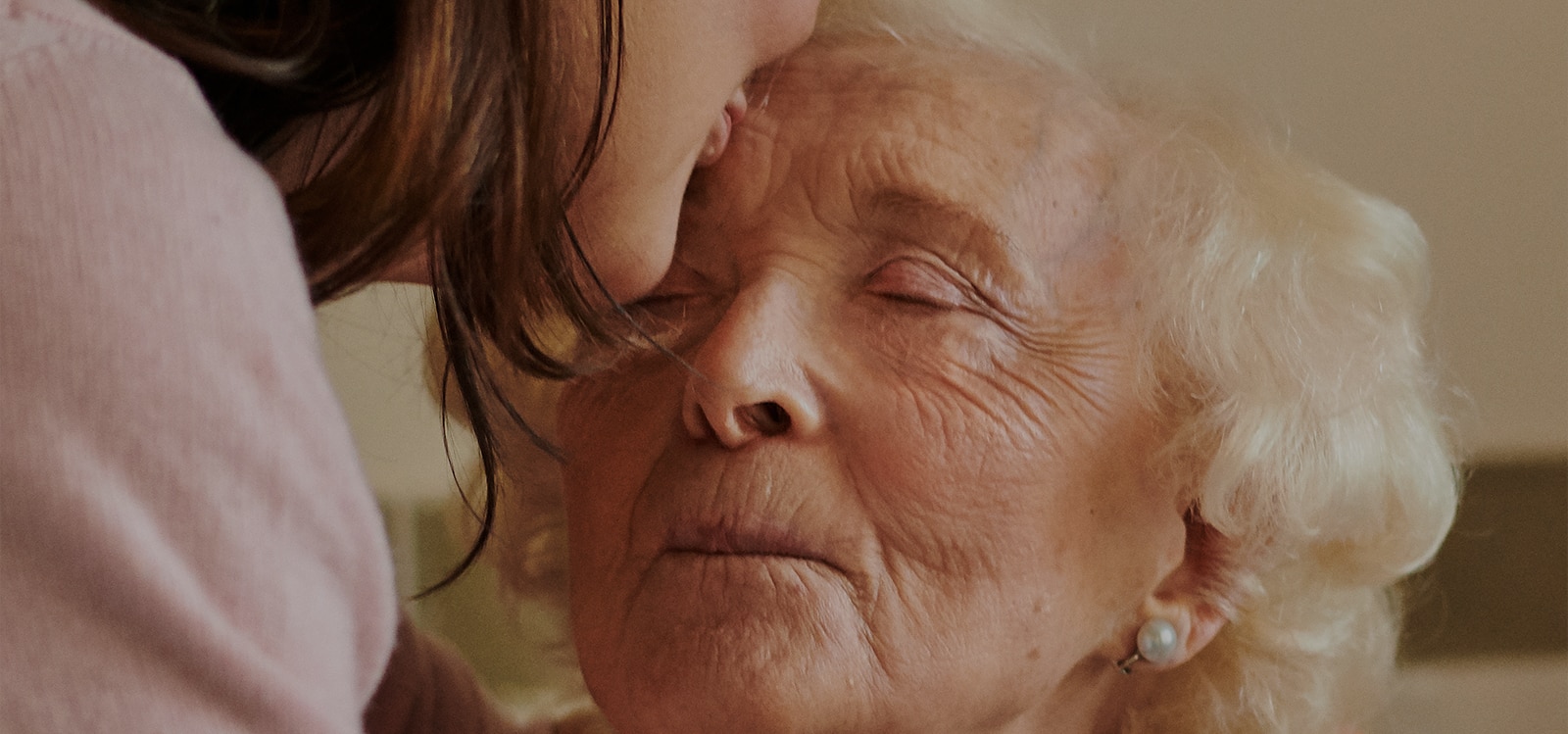 Elderly woman getting a kiss on the forehead from her carer. 