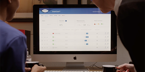 Two people looking at a screen with the TENA SmartCare interface displayed