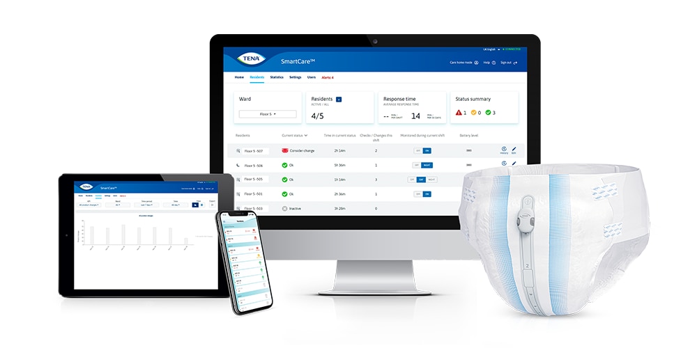 A computer monitor, tablet, and phone displaying a SmartCare dashboard next to a disposable diaper.