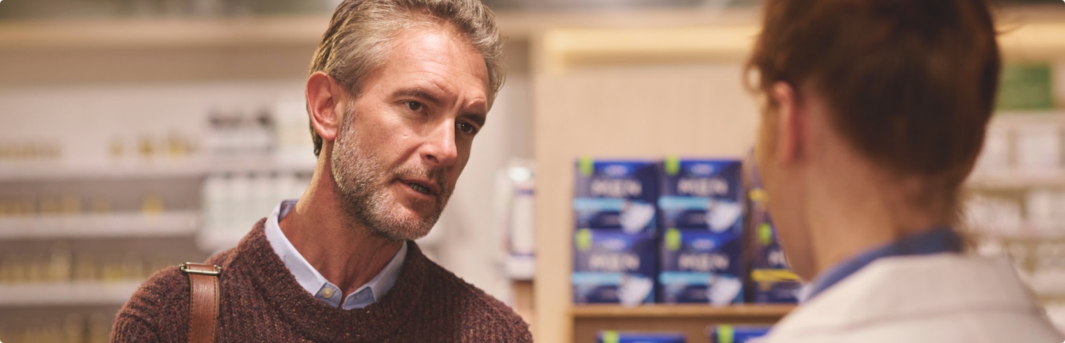 A pharmacist gives a male customer incontinence advice in a pharmacy