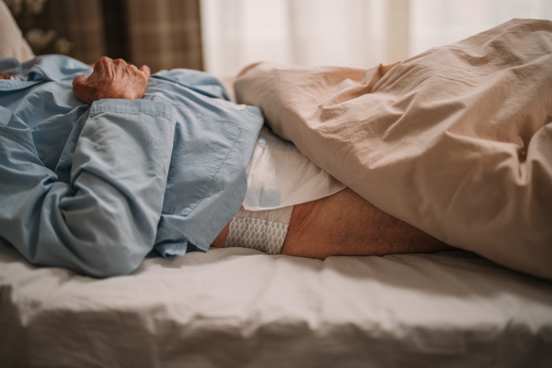 Äldre man som vilar i sängen iklädd ett TENA ProSkin Flex bälteskydd.