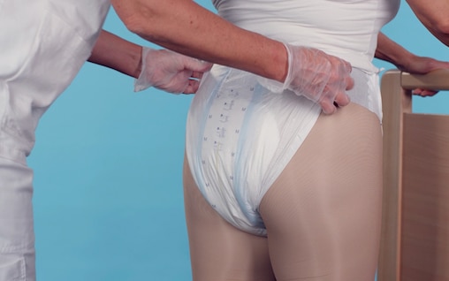 Snímek z videa o pečovateli, který obléká plenkové kalhotky TENA Flex stojícímu uživateli.